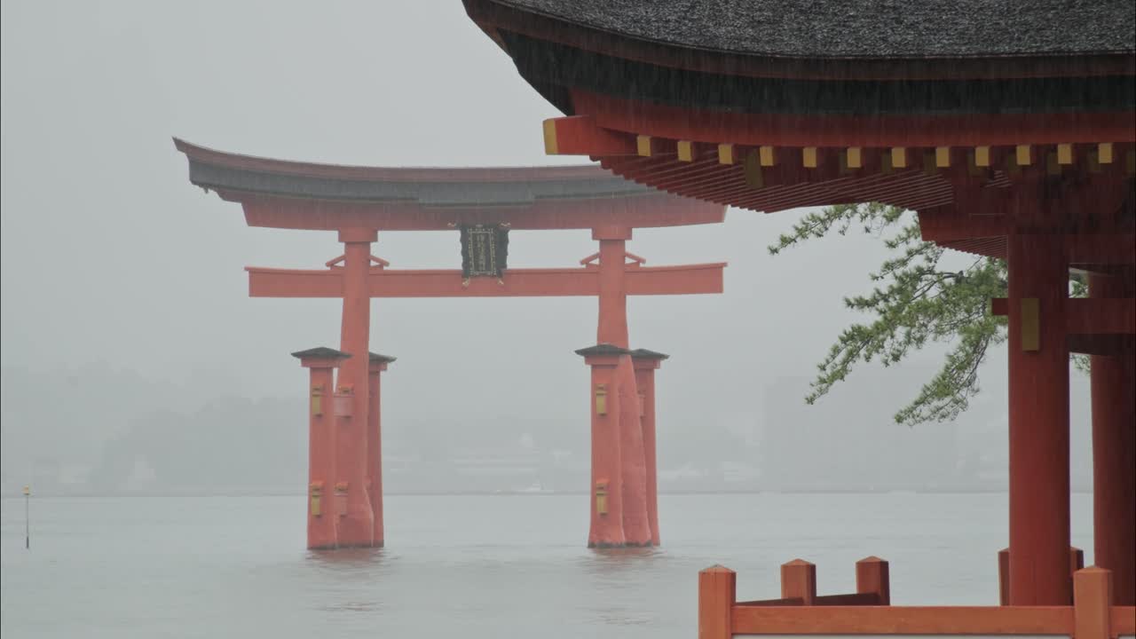 A close-up view of the Itsukushima Shrine torii gate during heavy rainfall on Miyajima Island, Japan. Mist and water blend to create a peaceful, sacred atmosphere.