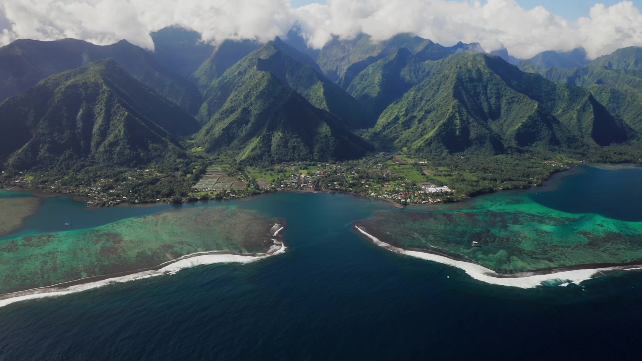 Aerial wide shot over a Teahupoo valley, Tahiti, mountains framing twin turquoise reef passes cutting through the coral reef into open ocean.