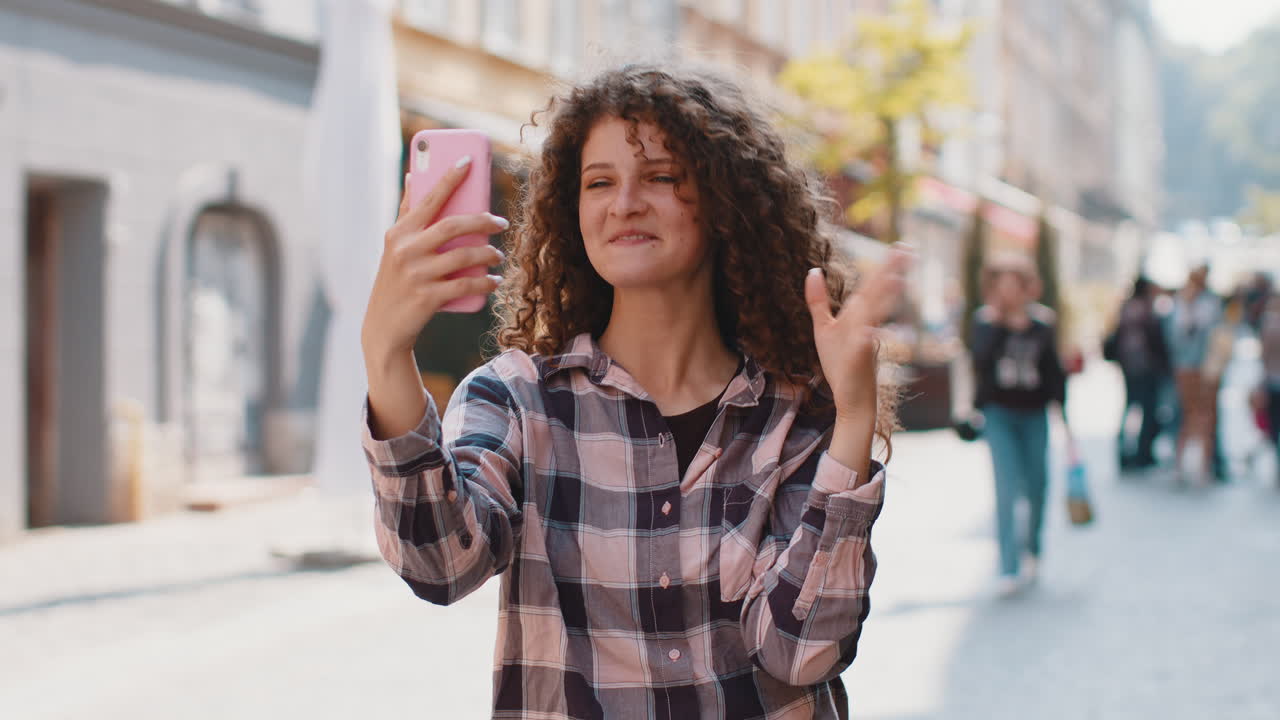 Young woman blogger taking selfie on smartphone video call online with subscribers in city street