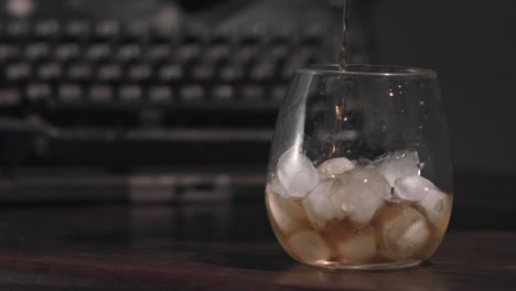 pouring wiske into the glass with ice, with a defocused typewriter on the background