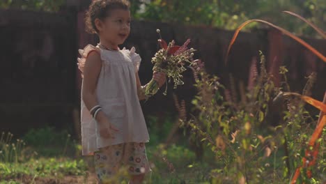 a pretty little girl collecting a bouquet of wildflowers as she walks around a garden outdoors in the sunshine picking flowers