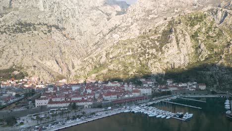 Drone-Dolley-Tilt-Shot-Del-Mar-Adriático-Con-La-Ciudad-De-Kotor-Entre-Las-Escarpadas-Montañas