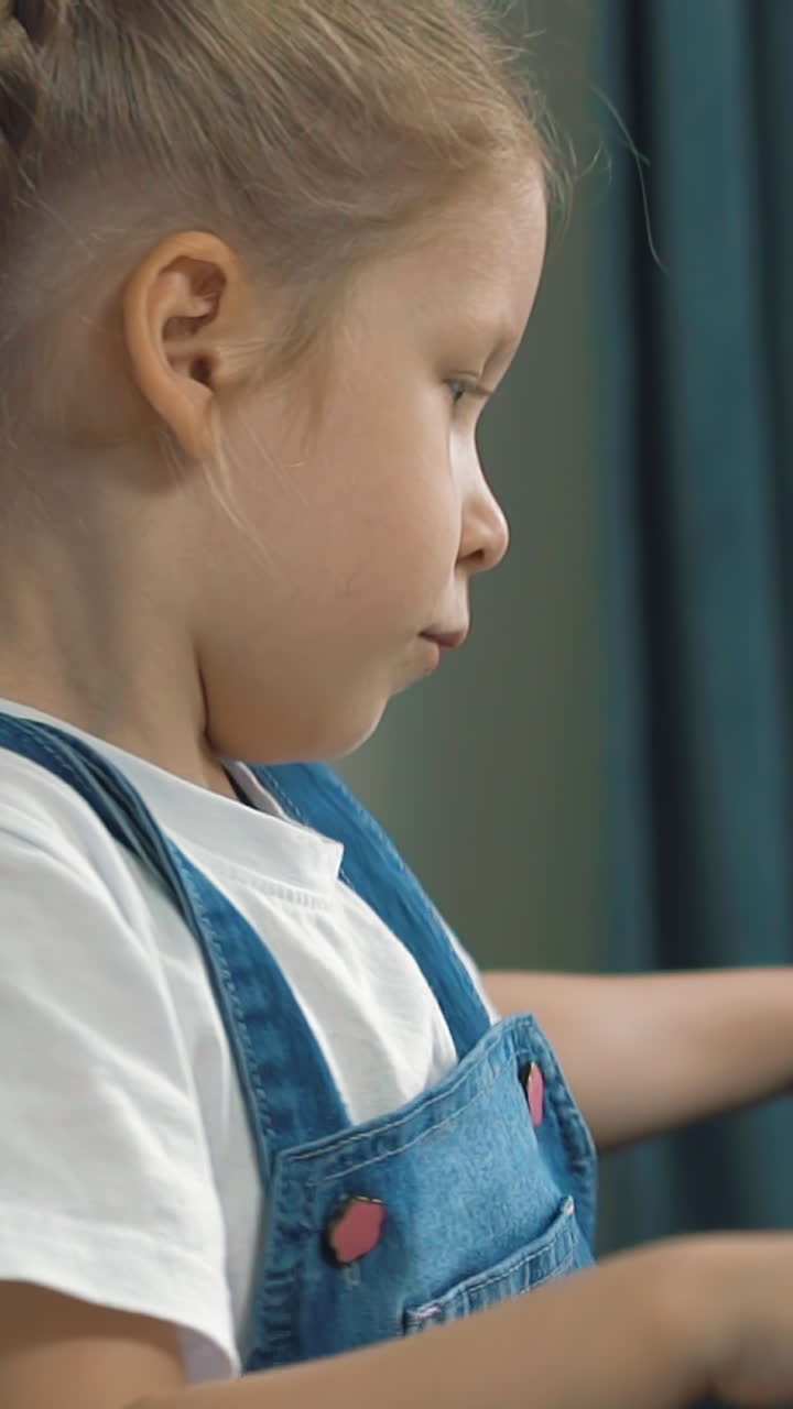 slow motion closeup side view portrait of little cute girl playing on dusty electric piano at home against backdrop of blue curtains during quarantine and pandemic