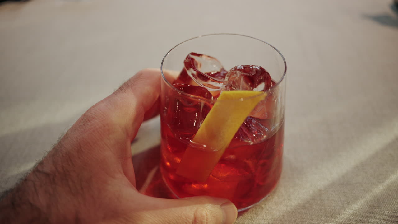 Primo piano di un uomo che tiene in mano un bicchiere da cocktail pieno di ghiaccio e una guarnizione di agrumi