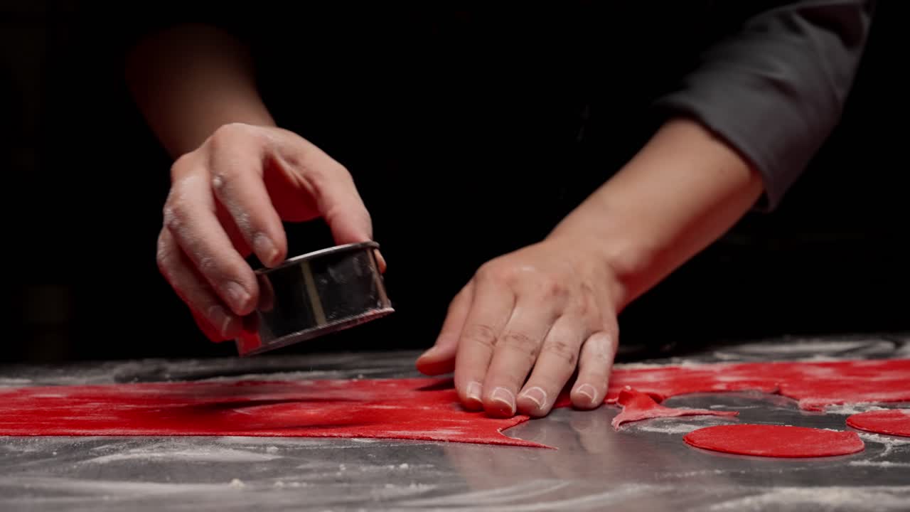 Primo piano di mani che tagliano l'impasto rosso con un tagliabiscotti rotondo