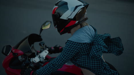 a lady rides a red power bike along a tarred road, her shirt billowing in the wind and exposing part of her body as she leans forward, gripping the handlebar