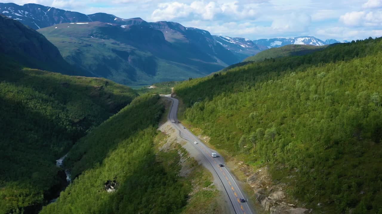 Aerial view overlooking RV and cars, driving on a mountain road, Arctic fells in the background, sunny day, in Norway - rising, drone shot
