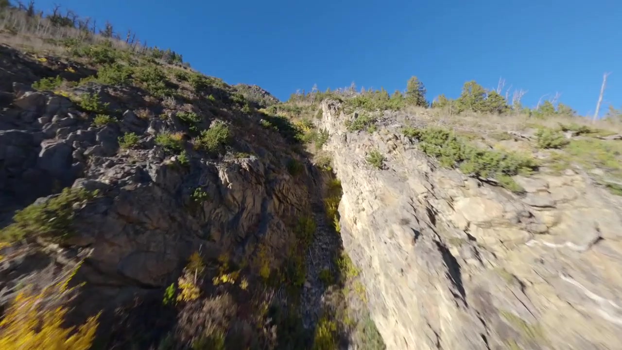 Grabación de dron FPV de alta velocidad, volando rápido y bajo por una grieta en la ladera rocosa de una montaña, mostrando un terreno dramático y un movimiento emocionante