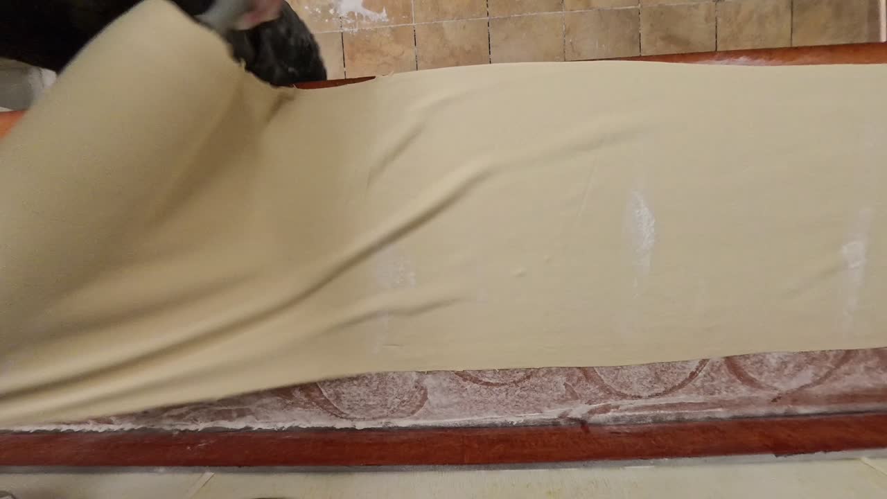 Geniş bir masanın üzerine açılan pizza hamuru.