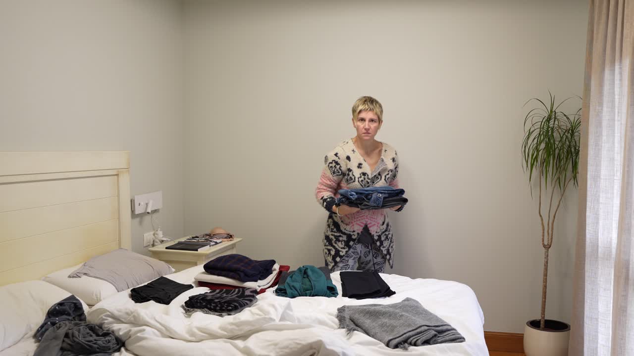 Una donna sta piegando dei vestiti su un letto in una camera da letto