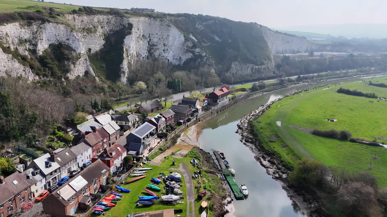 Discesa aerea con drone su Lewes, Sussex, Inghilterra fino al fiume Ouse con barche, abitazioni lungo il fiume e scogliere bianche. Movimento cinematografico fluido che rivela la periferia della città e dettagli del paesaggio rurale