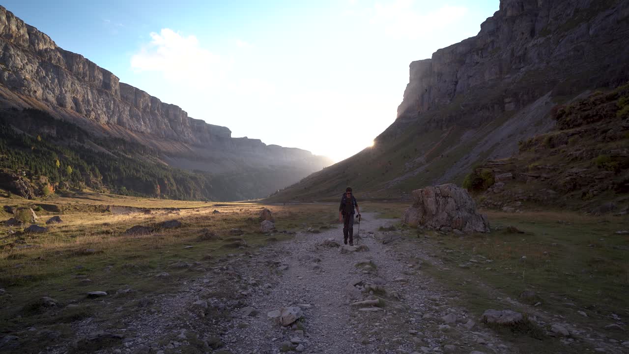 vista frontal de un joven excursionista caminando hacia el sol en el parque nacional del valle de ordesa, pirineos, huesca, españa