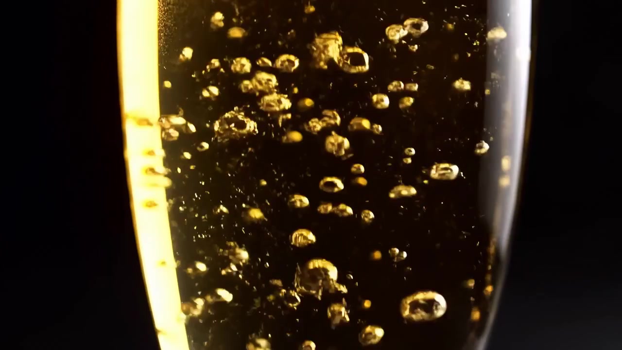 Scena ravvicinata in movimento di bollicine dorate che salgono all'interno di un bicchiere alto e slanciato di liquido ambrato, con riflessi luminosi, un sottile anello di schiuma in superficie, illuminazione laterale calda e un'elegante atmosfera da studio