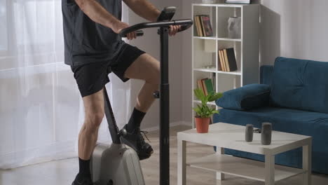 training with stationary bicycle in home conditions man is spinning pedals in living room workout for keeping fit and health