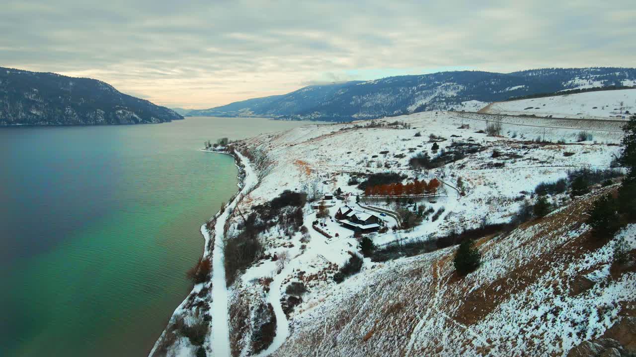 Ilmakuva Wood Lake -järvestä Kelownassa: Ylhäältä otettu näkymä turkoosista vedestä ja lumipeitteisistä punaisista kallioista rannan varrella.
