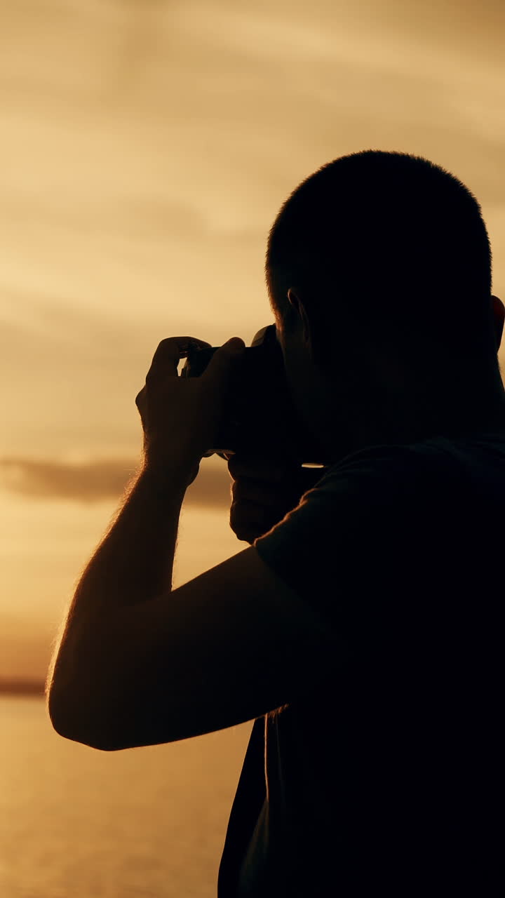 a man looks at the photos in the camera near the river at sunset. The guy chooses the best photos. Vertical video