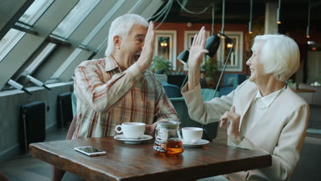 senior couple high-fiving and enjoying tea at a cafe