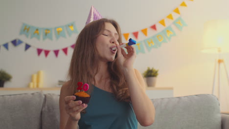 woman blowing out candles on her 20th birthday cupcake