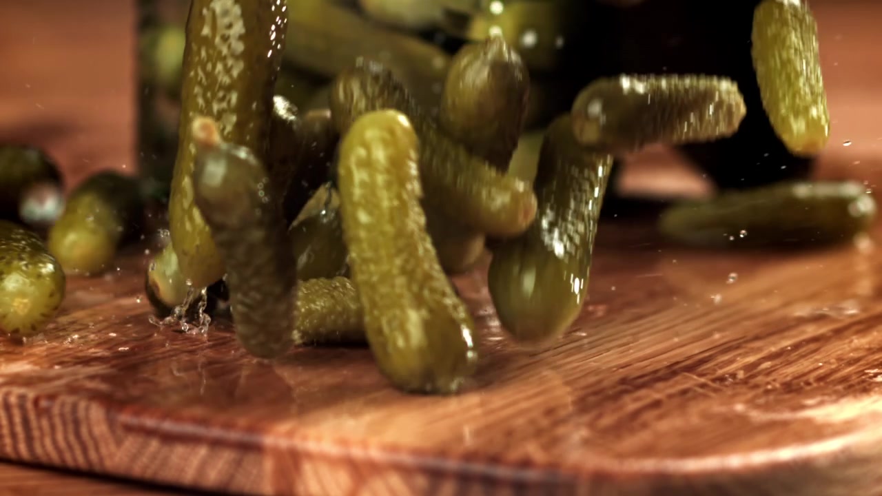 Cornichons marinés tombant au ralenti sur une planche en bois humide