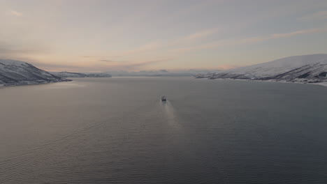 bird's eye view of cargo boat cruising in fiord between snowy islands in tromso, norway