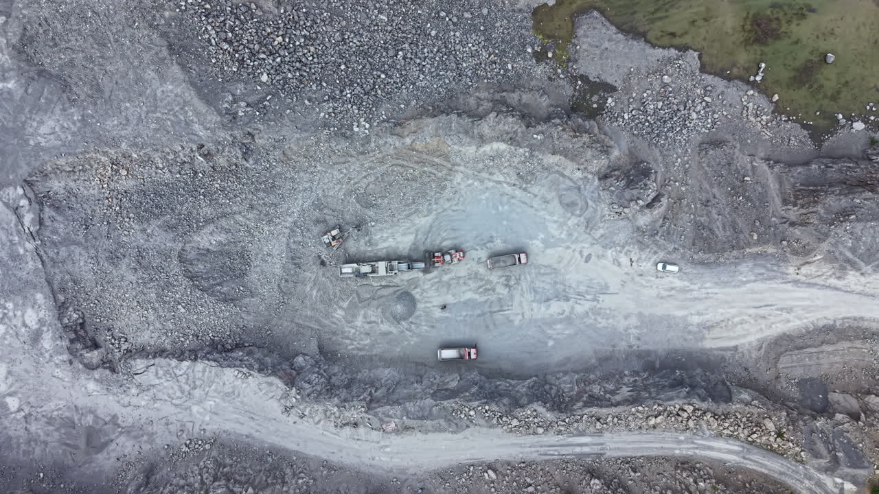 Heavy machinery works on gravel extraction site in a remote area with large rocks and rough terrain during daylight hours