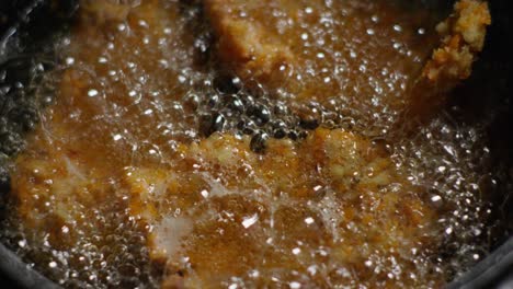 crispy golden fried chicken boiling in hot oil with frying bubbles, close up top down