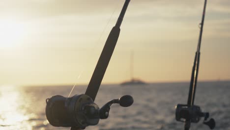 camera pans from the tip of a fishing rod to the reel mounted on a boat during golden hour.