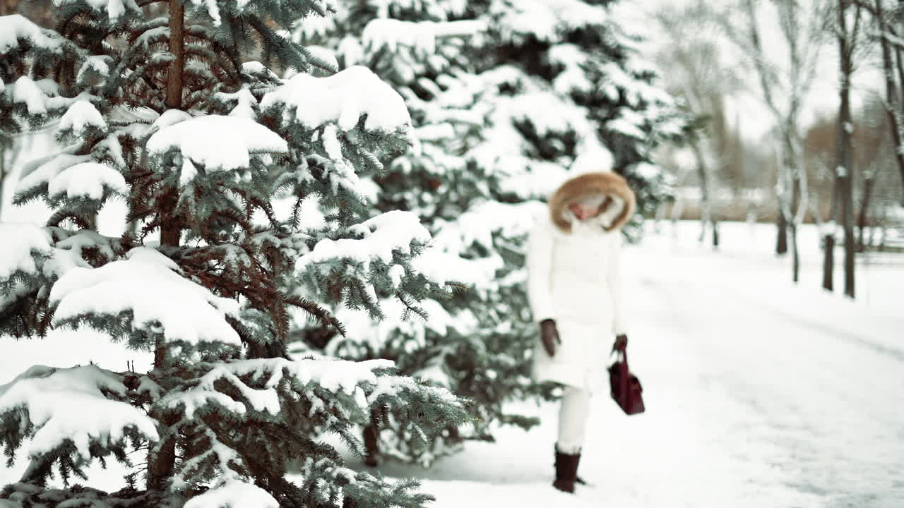Woman wearing white winter coat playing with snow near pine trees