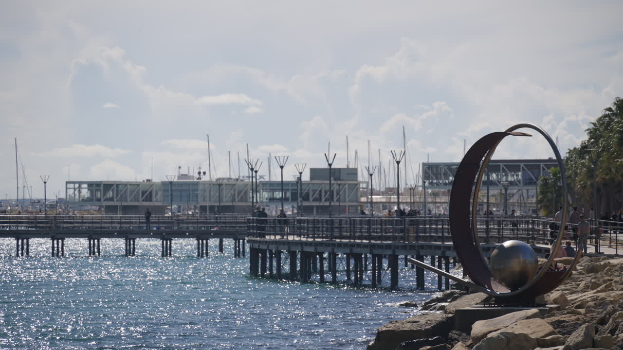 Limassol, Cyprus - February 26, 2026: View of a coastal pier with calm water and marina structures in Limassol with a circular metal sculpture