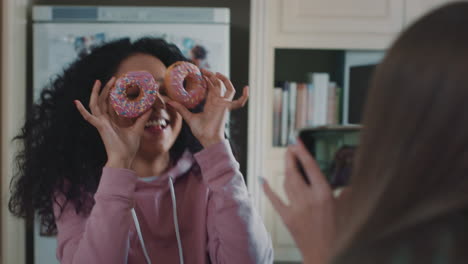 funny teenage girls posing with donuts taking photos using smartphone sharing on social media enjoying hanging out on weekend in kitchen