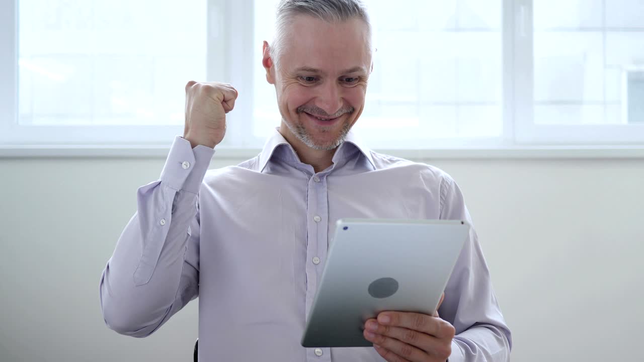 hombre de mediana edad emocionado por el éxito mientras usa la tableta