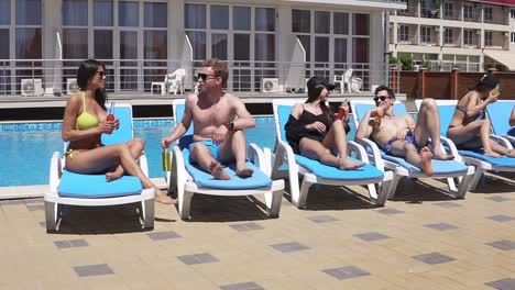 happy young people lying on sunbeds by the swimming pool and having fun