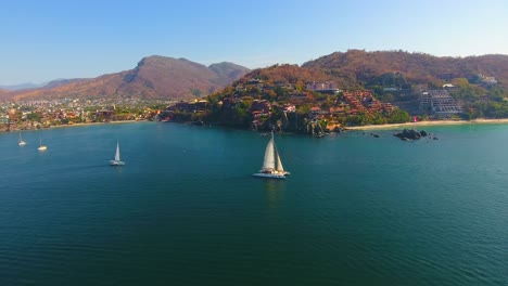 drone video slowing orbiting around a catamaran sailboat cruising around a beautiful urban point in mexico in a beautiful ocean bay