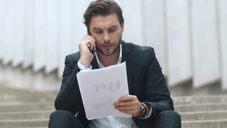 Businessman-having-conversation-on-cellphone-at-street.-Man-sitting-on-stairs