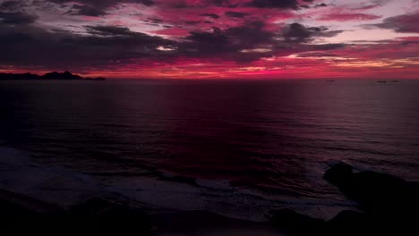 Intensiver-Roter-Und-Magentafarbener-Bewölkter-Seelandschaftshimmel-Kurz-Vor-Sonnenaufgang-Mit-Den-Wellen-Im-Dunkeln-Im-Vordergrund,-Die-Am-Teufelsstrand-In-Rio-De-Janeiro-Eintreffen