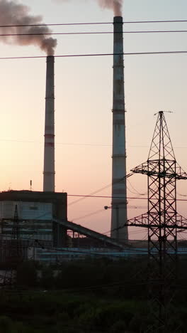 panoramic view on harmful power station at sunset. tall electricity pylons next to large factory with smoke stacks on the evening sky. camera rising up. vertical video
