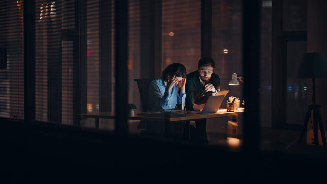 Overloaded partners brainstorming night office looking laptop. Two colleagues