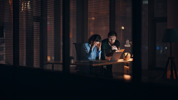 Partner oberati di lavoro che fanno brainstorming di notte in ufficio guardando un portatile. Due colleghi