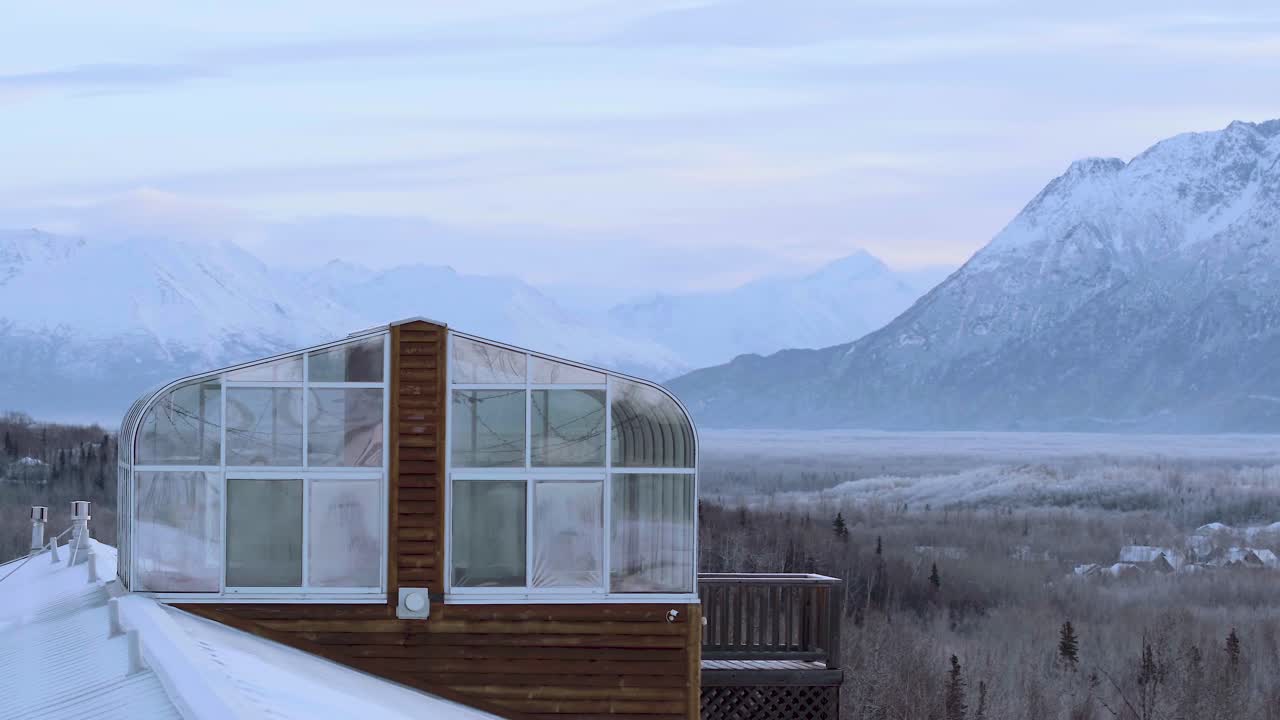cabaña de alaska con solárium en el techo, vista aérea que revela un amplio valle con casas en el bosque