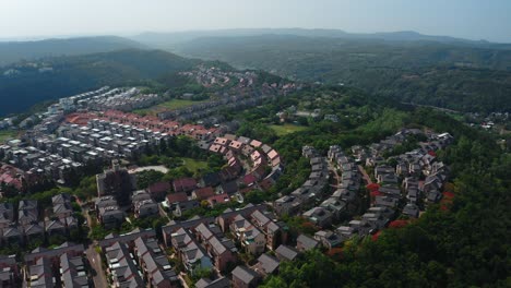 aerial forward view of housing area with apartments surrounded by green hilly landscape in china during foggy day - suburban district in china