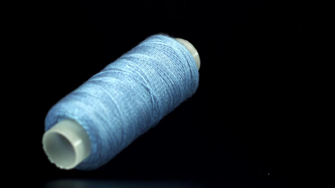 Light Blue Thread Spool Falling and Landing on Black Background in Slow Motion