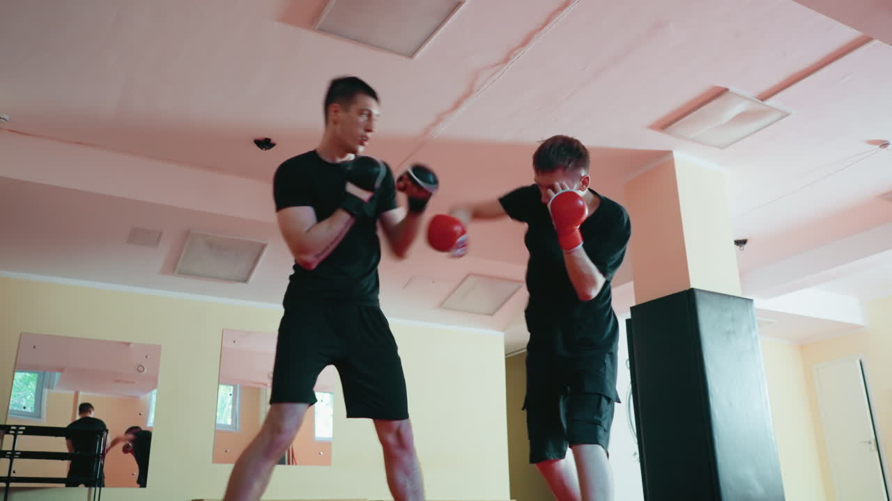 Karate practitioners sparring inside dojo on red mat, wearing protective gloves, engaged in close range combat training, showing focus, movement, reaction, balance, and determination during practice