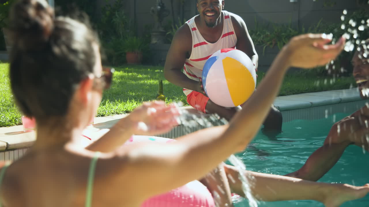 Amigos diversos curtindo uma festa na piscina, rindo e espirrando água em um dia ensolarado.