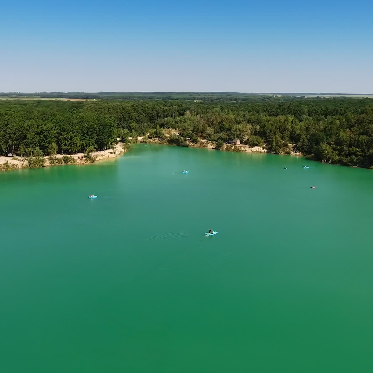 Beautiful scenery of a blue lake surrounded by rocky bank with green forests. Blue skies reflecting in the water. Aerial view