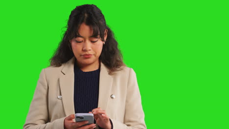 close up studio shot of businesswoman using mobile phone to message or browse online standing against green screen