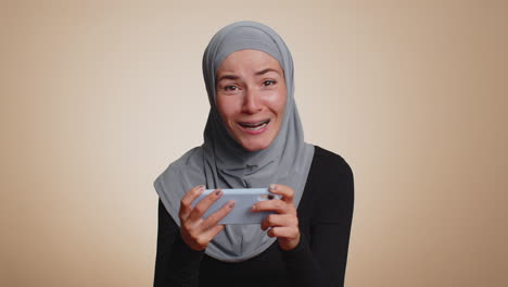 Worried-funny-addicted-muslim-girl-enthusiastically-playing-drive-racing-video-game-on-mobile-phone