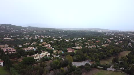 Drohne-Fliegt-über-Kleine-Vorstadt-In-Hügeln-Und-Landschaft,-Spanien