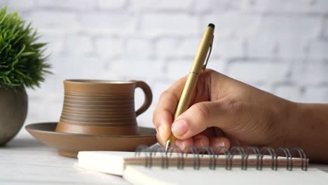 person writing notes in notebook at desk with coffee