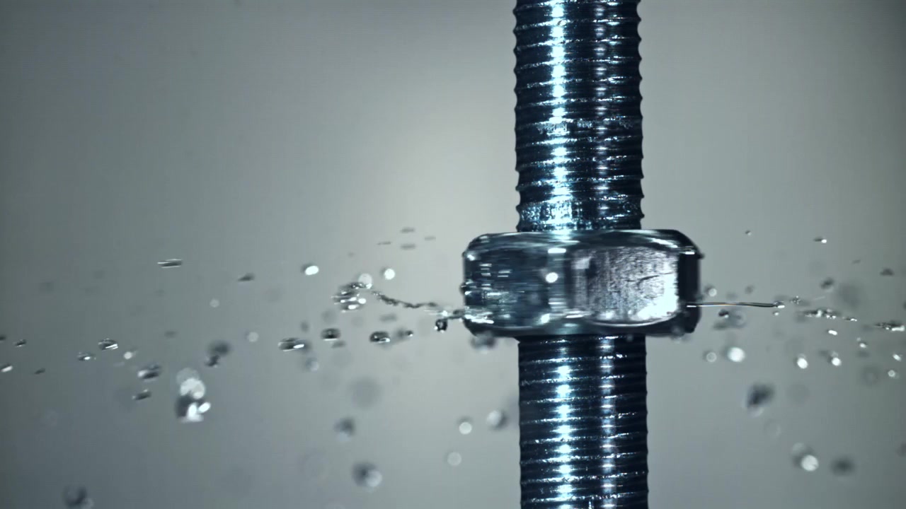 Primo piano di un dado metallico che gira su un bullone con schizzi d'acqua