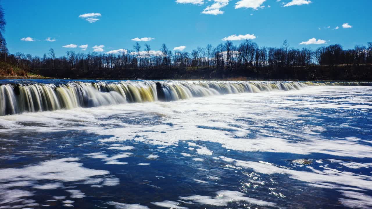 Spring sunlight glistens on wide waterfall as slow zoom reveals full natural span